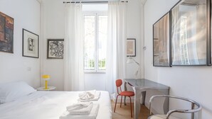 A hotel room with a bed, a desk, two chairs, and artwork on the walls. - Elegantis.it Des Artistes Apartment (Roma)