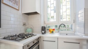 A kitchen with white cabinets, a gas stove, a kettle, a coffee maker, and a fruit bowl. - Elegantis.it Des Artistes Apartment (Roma)