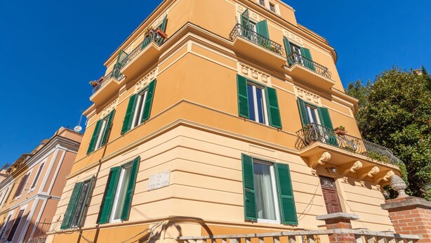 A multi-story building with green shutters, a sign indicating 'VIA PORTA MACCIARE,' and a clear blue sky in the background. - Elegantis.it Des Artistes Apartment (Roma)