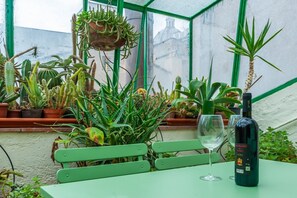 A greenhouse with various cacti and succulents, a bench, a table with a wine bottle and glass, and a view of buildings through a green-framed window. - Elegantis.it Architect's House in Campo dè Fiori (Roma)