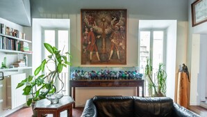 A living room with a large painting, a glass display case with decorative items, a leather sofa, and a bookshelf. - Elegantis Dimora dell'Architetto in Campo de' Fiori With private terrace (Roma)