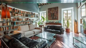 A spacious living room with a large bookshelf, leather sofas, and a painting on the wall. - Elegantis Dimora dell'Architetto in Campo de' Fiori With private terrace (Roma)