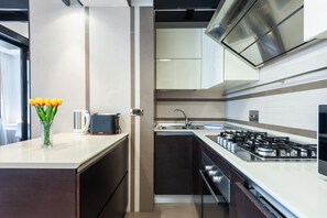 Una cocina moderna con estufa a gas, electrodomésticos de acero inoxidable y un florero con flores amarillas sobre la encimera.