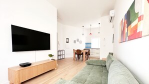 A modern living room with a flat-screen TV, a wooden console, a green sofa, and a dining area with a table and chairs. - Elegantis Santa Croce Suite Apartment (Roma)