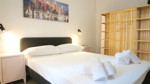 A neatly made bed with white linens, a headboard, and a nightstand with a lamp. - Elegantis Santa Croce Suite Apartment (Roma)