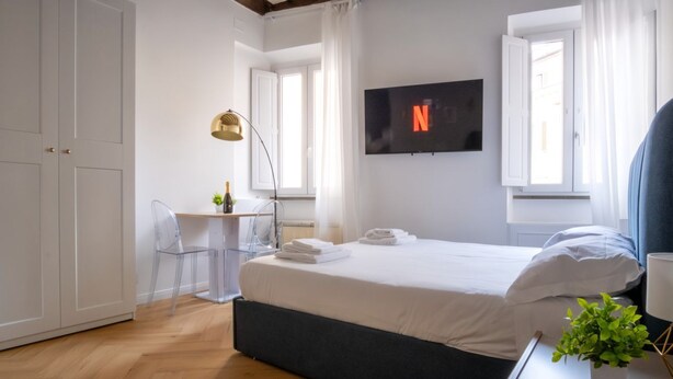 A modern hotel room with a bed, a desk, a chair, a TV, and a window.
