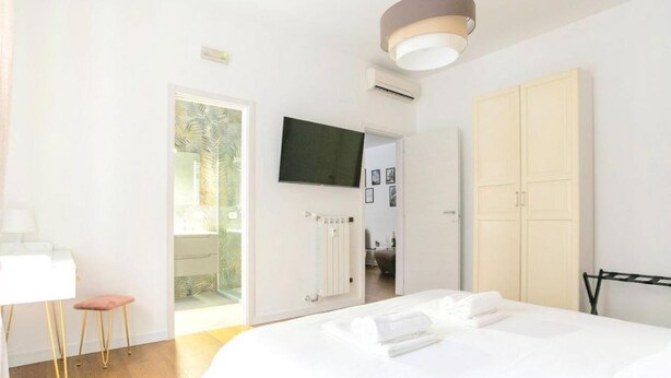 A bedroom with a bed, a desk, a chair, a wardrobe, and a television.