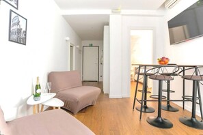 Et moderne værelse med sofa, et lille bord med en flaske og glas, samt en bar med barstole.