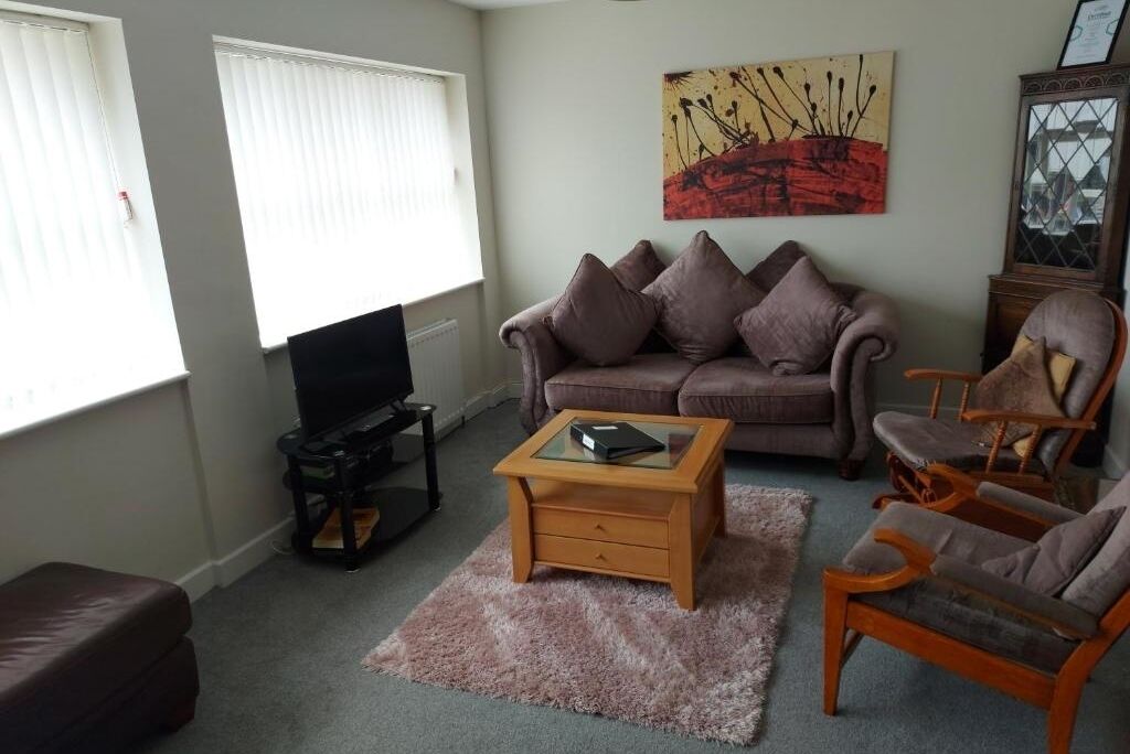 Un salon avec un canapé, des fauteuils, une table basse, un téléviseur et un tableau accroché au mur.