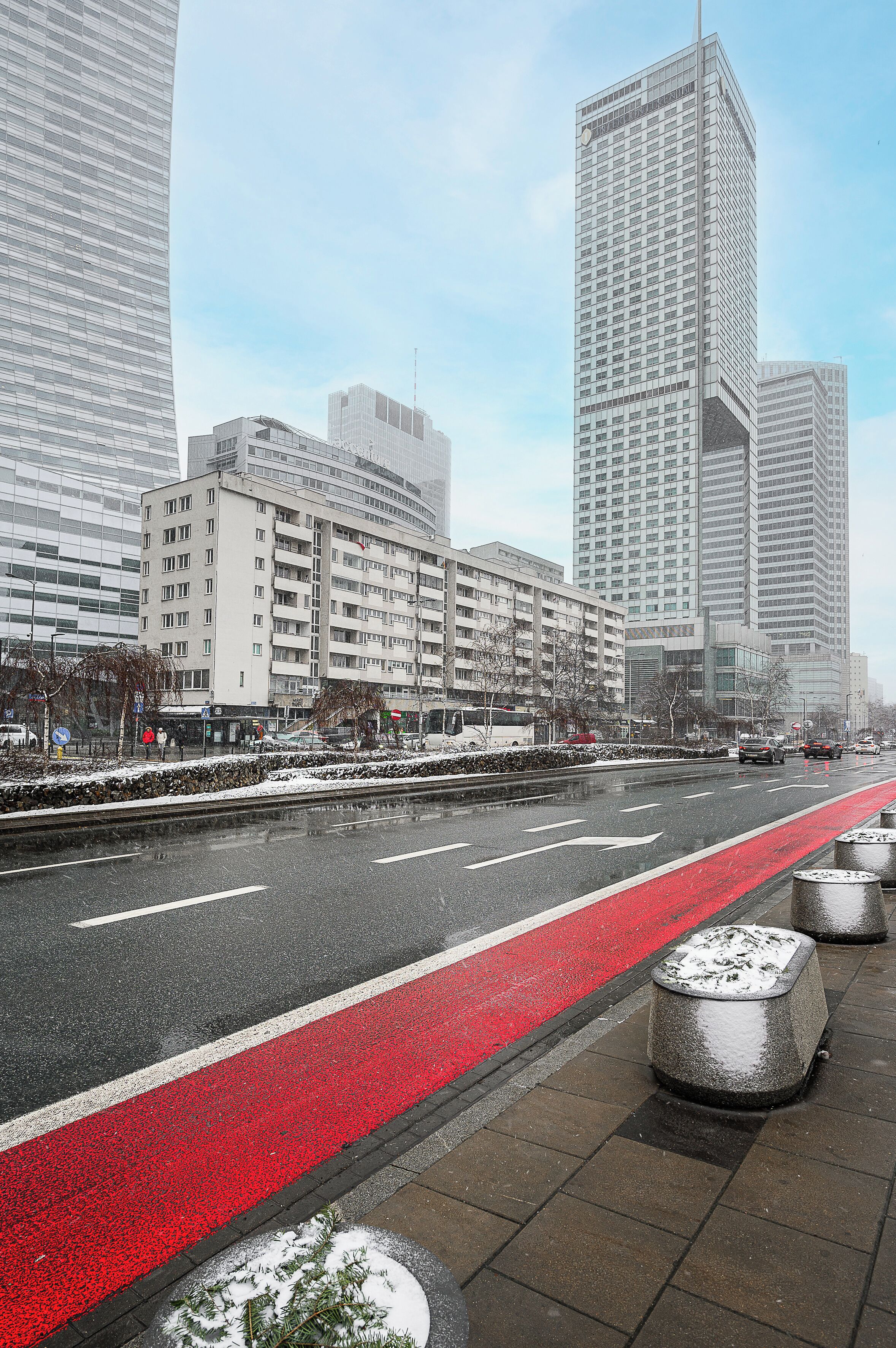 Eine Stadtstraße mit modernen Gebäuden, einer roten Fahrradspur und Schnee auf dem Boden.
