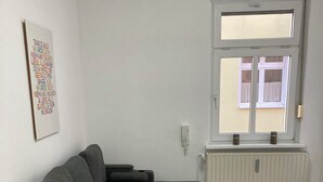 Een moderne woonkamer met een grijze modulaire bank, een klein rond tafeltje met houten poten en een radiator bij een raam.