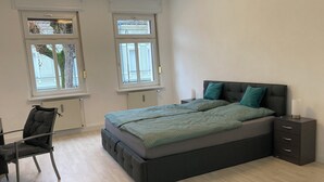 Een slaapkamer met een groot bed, twee nachtkastjes, een stoel en twee ramen.