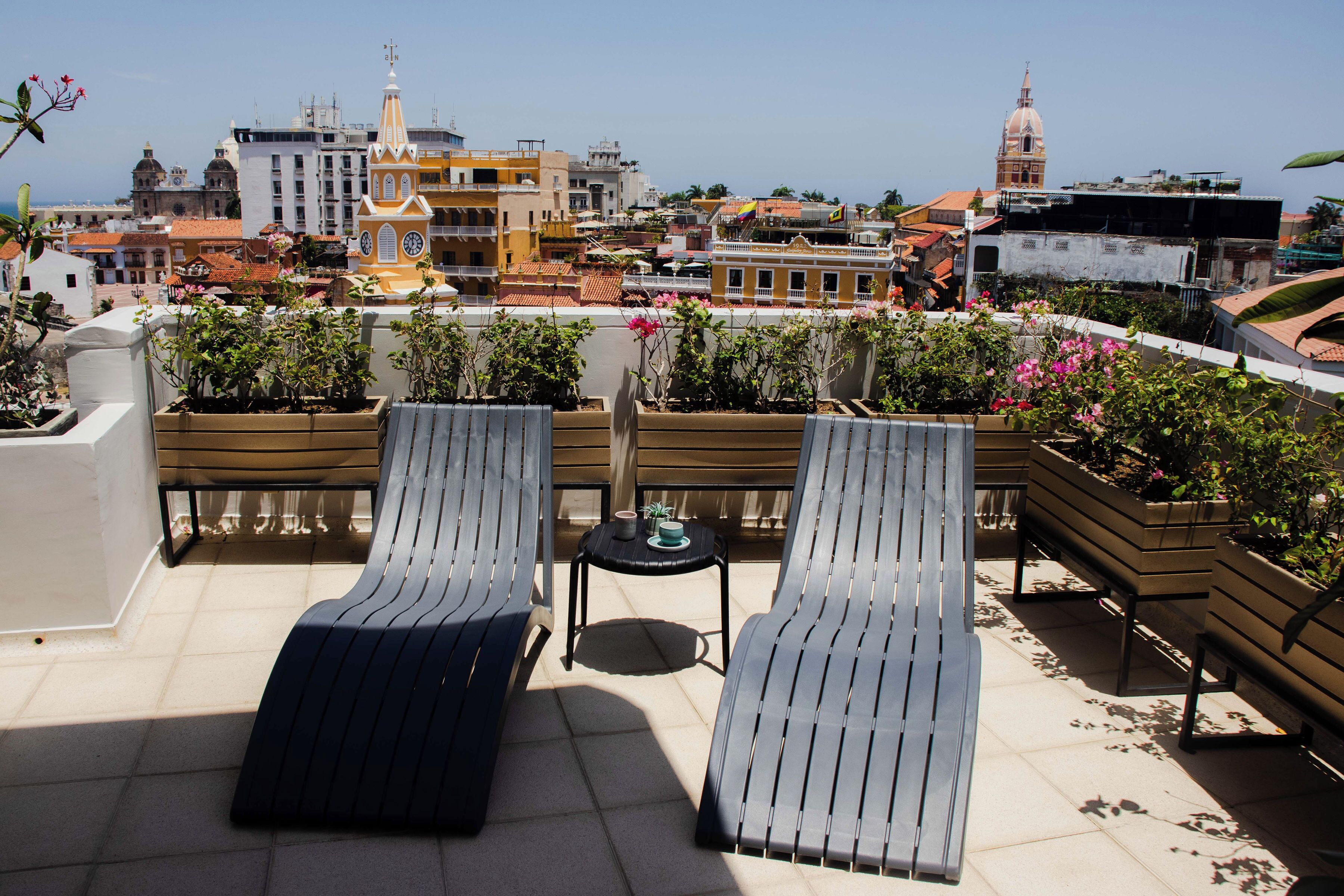 A rooftop terrace with two lounge chairs and a small table, overlooking a cityscape with historic buildings and a clock tower.