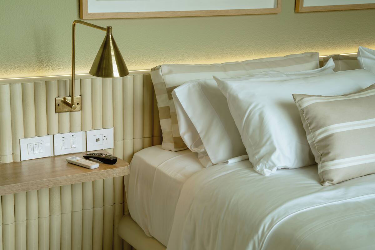 A neatly made bed with white bedding and a bedside table with a remote control.