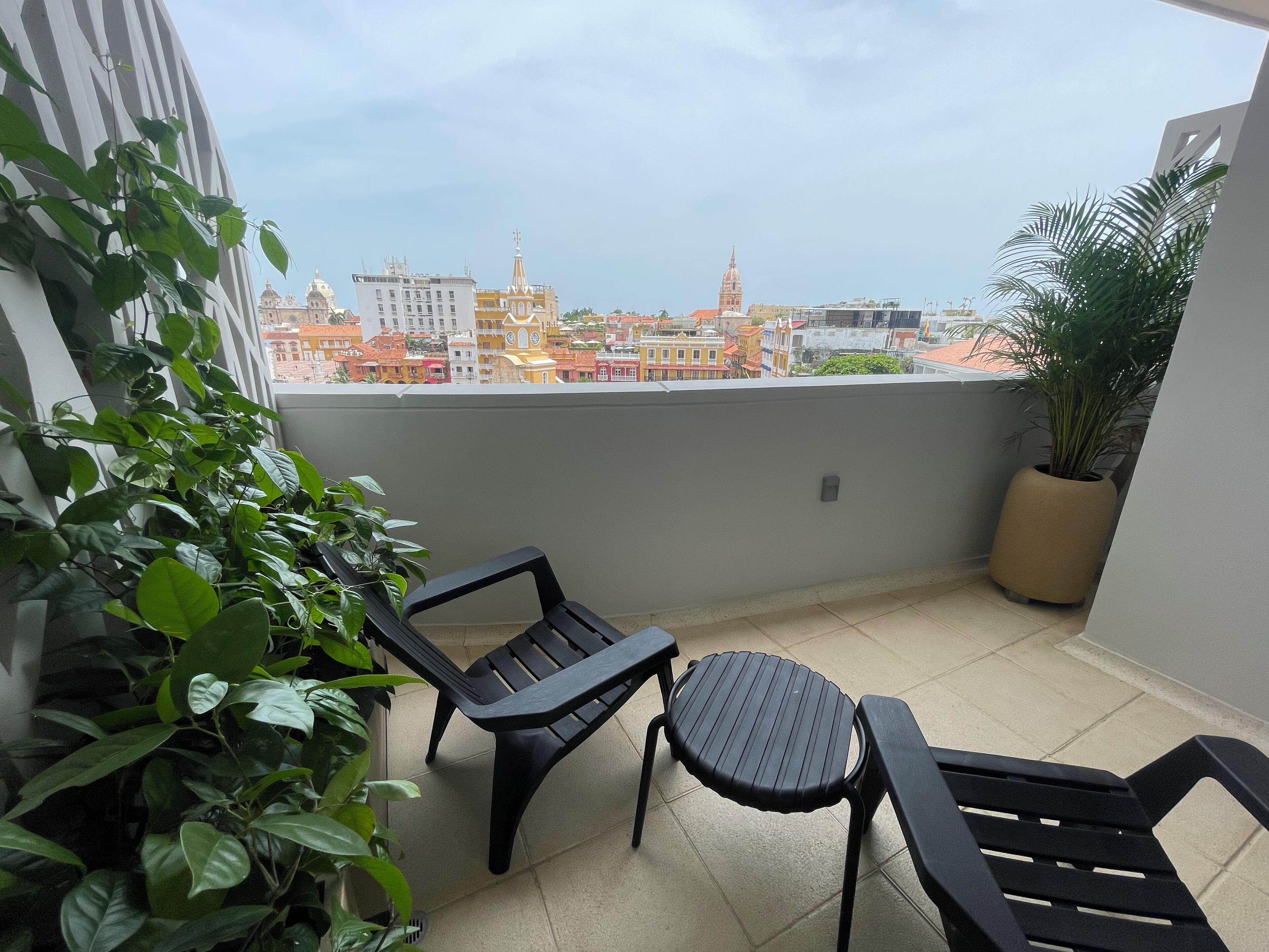 Un balcone con due sedie di plastica nera, una pianta in vaso e vista su edifici colorati.