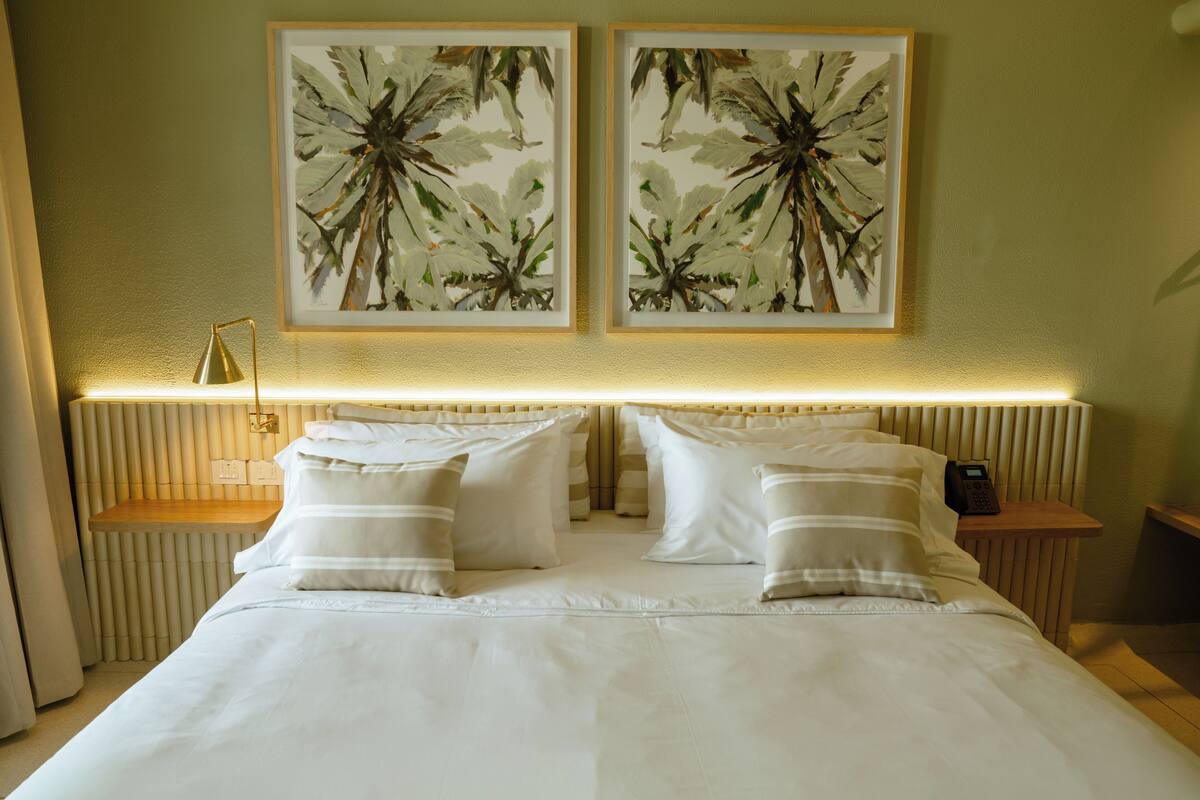 A hotel room with a neatly made bed, two bedside tables with lamps, and two framed floral paintings on the wall.