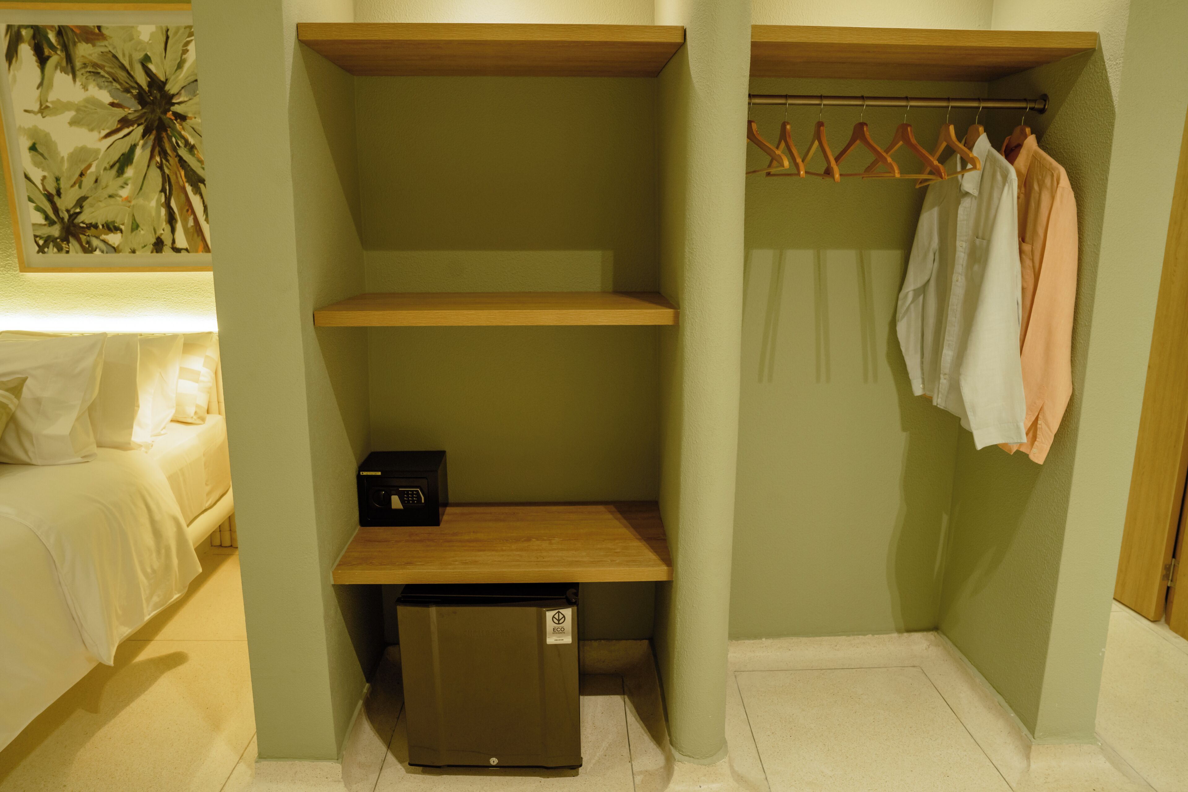 A compact room with a bed, a small wooden desk, a trash bin, and a clothing rack with hangers.