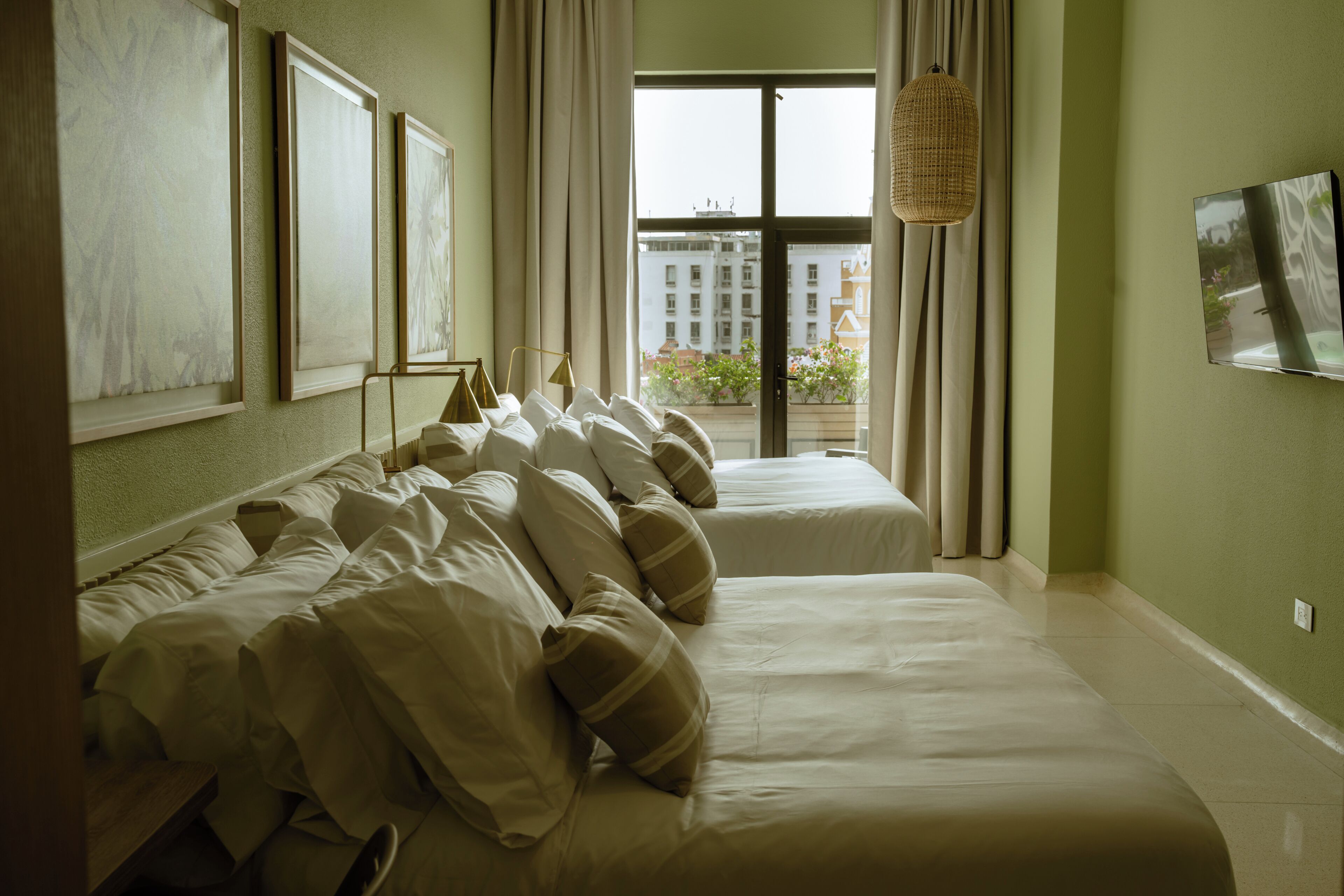 A hotel room with two beds, a large window with curtains, and artwork on the walls.