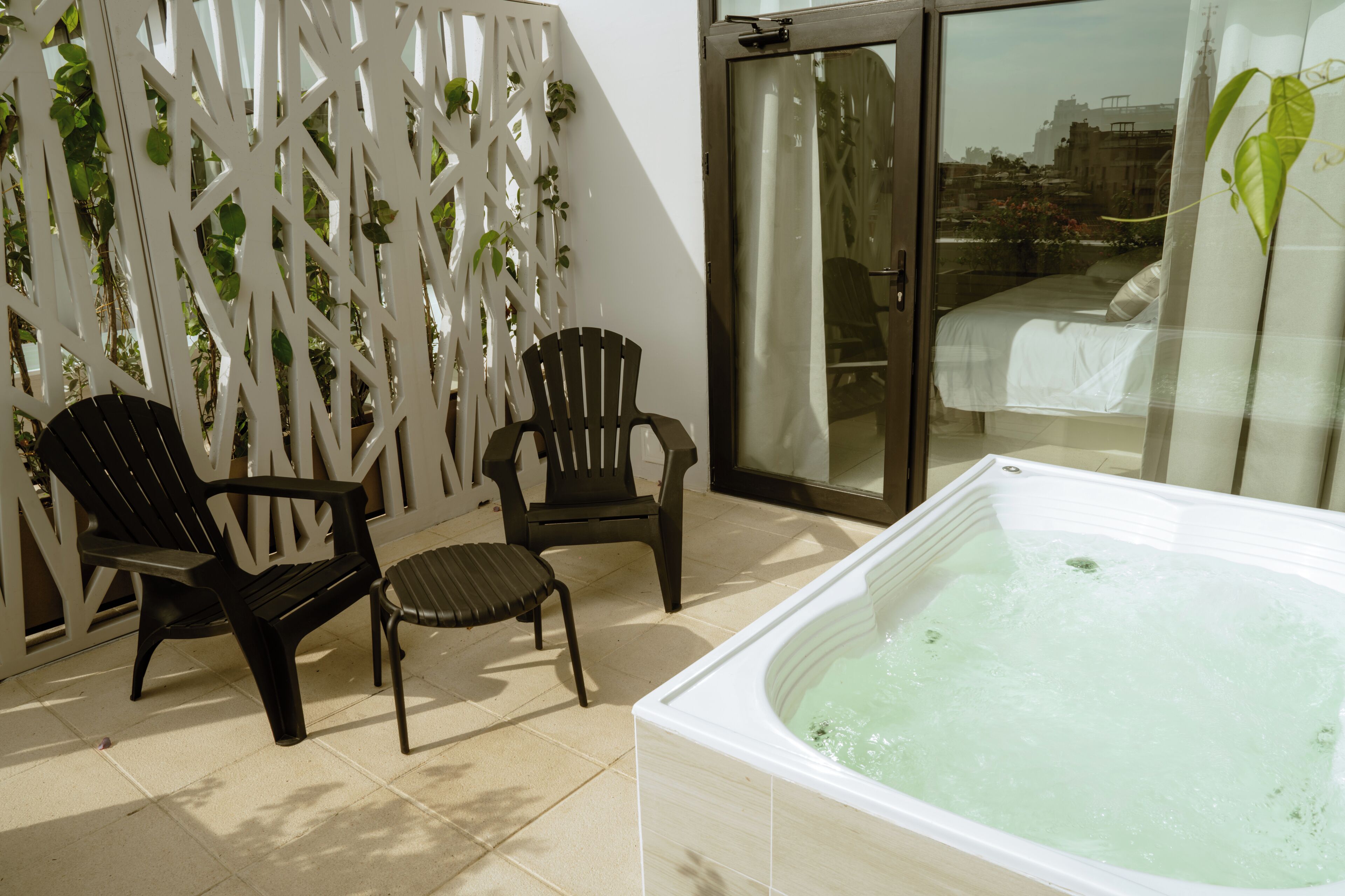 A balcony with a hot tub, two chairs, and a white lattice partition with greenery.