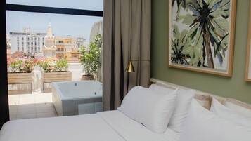 A hotel room with a bed, a painting, a view of a cityscape, and a balcony with flowers.