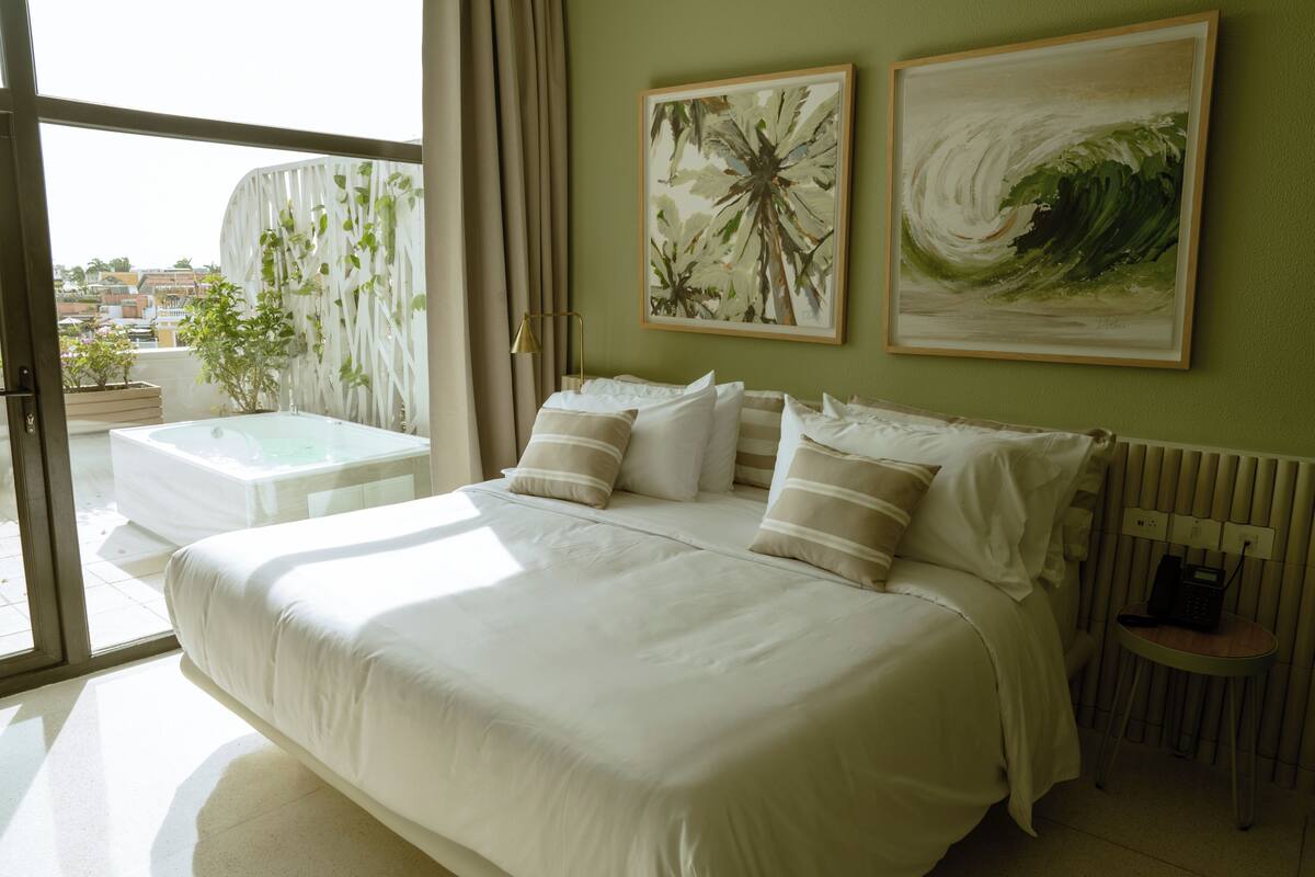 A hotel room with a large bed, a small table, and two paintings on the wall.