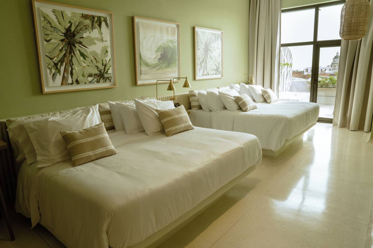 A hotel room with two beds, a large window, and artwork on the walls.