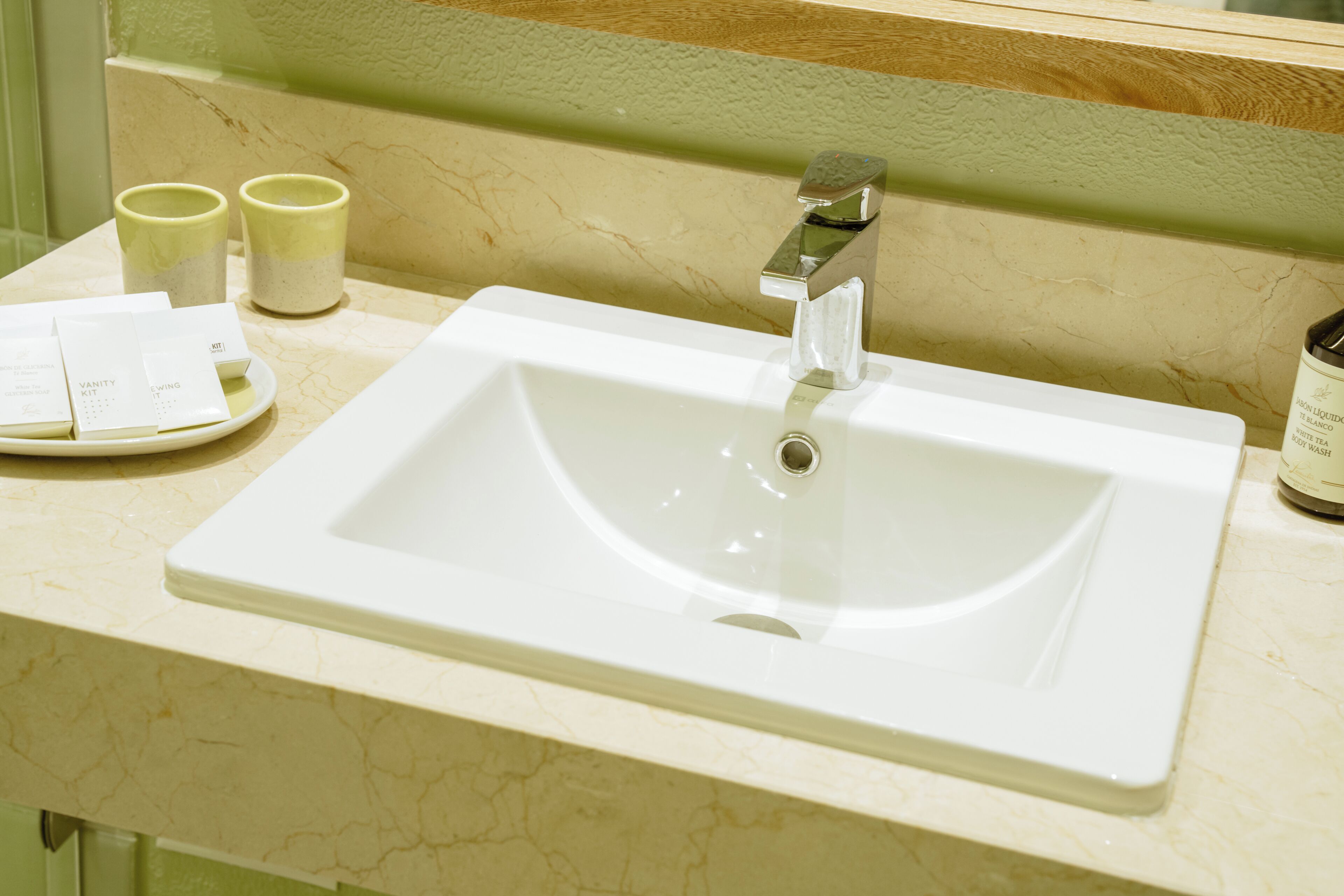A bathroom sink with a mirror above it, a plate with toiletries, and two cups on the counter.