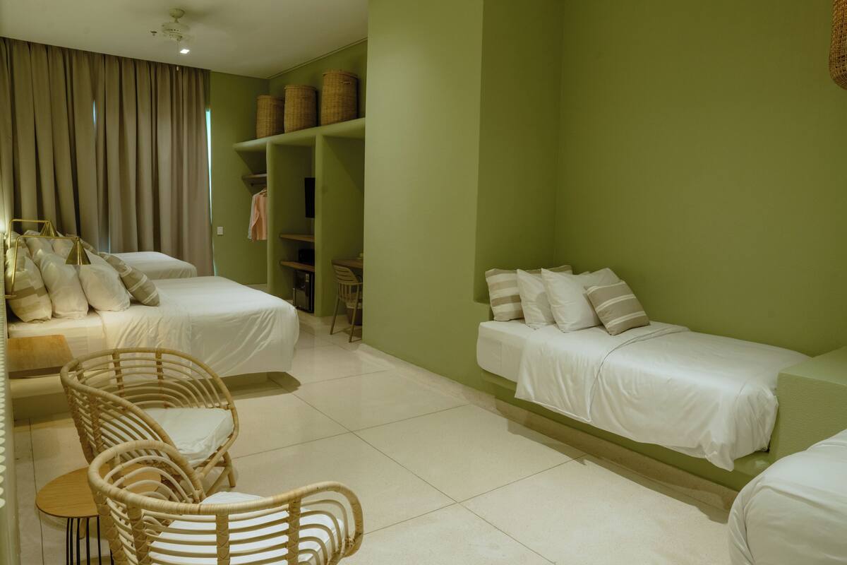 A room with two beds, wicker chairs, a small table, and a wardrobe with baskets.