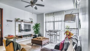 A modern living room with a TV, sofa, dining table, and ceiling fan.