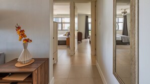 A hallway with a mirror, a vase with flowers, and a bed in the distance.