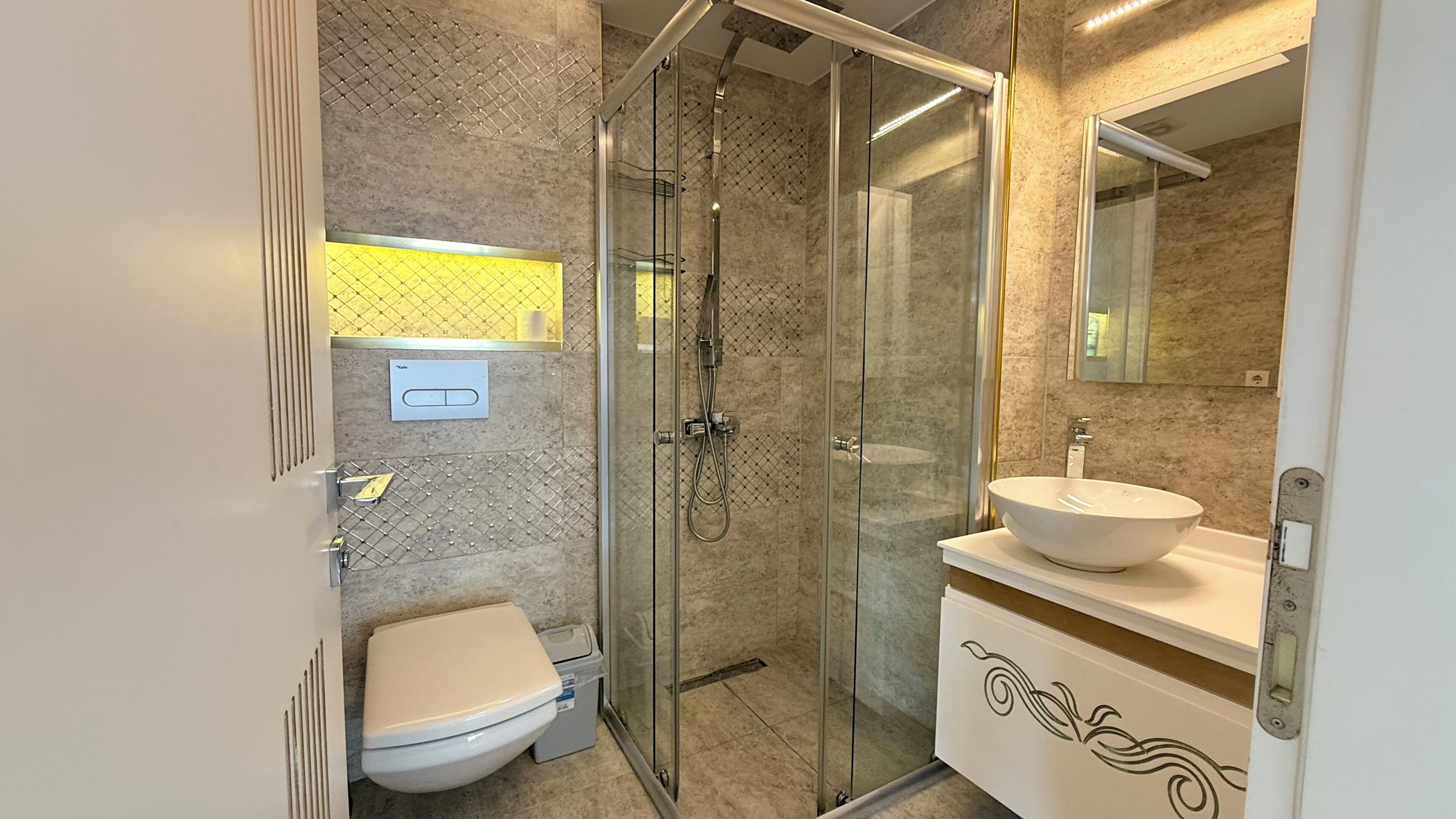 Un baño moderno con ducha envuelta en vidrio, inodoro y lavabo con un mueble decorativo.
