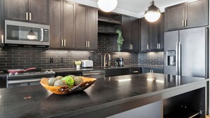 Una cocina moderna con armarios oscuros, electrodomésticos de acero inoxidable y una isla central con un frutero.