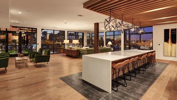 Una cocina moderna con una isla grande, taburetes de bar y vistas a la ciudad al atardecer.
