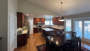 Een moderne keuken met houten kastjes, een centraal eiland en een eethoek met een grote tafel en stoelen.