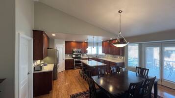 A modern kitchen with wooden cabinets, a central island, and a dining area with a large table and chairs.