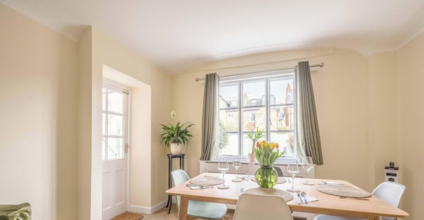 A dining area with a table set for four, a potted plant, and a window with curtains.