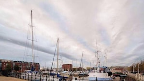 Een jachthaven met meerdere boten afgemeerd, een gebouw met een rode gevel, en een bewolkte lucht.