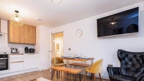 Een moderne keuken met witte kastjes, een zithoek met een houten tafel en stoelen, en een zwarte leren fauteuil.