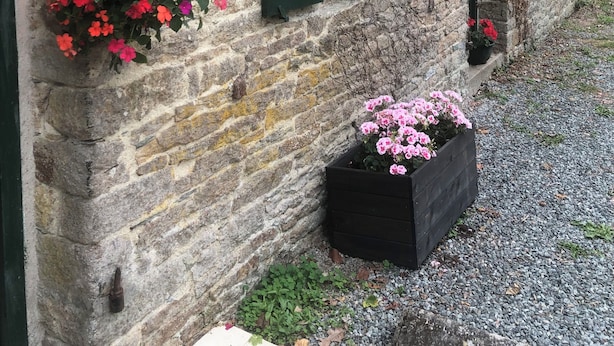En rustik bygning i sten med grønne skodder og blomsterkasser.
