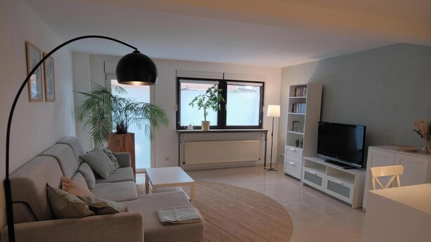 A modern living room with a sofa, a small table, a TV, and a bookshelf. - Quiet apartment for commuters & nature lovers - parking lot (Duisburg)