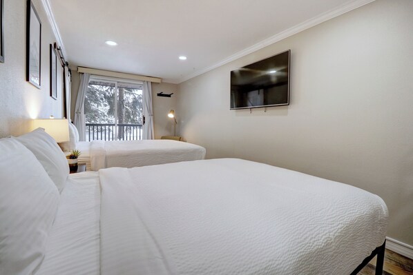 A bedroom with two beds, a TV, and a window with curtains.