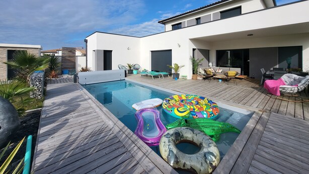 A modern outdoor pool area with a wooden deck, lounge chairs, and inflatable toys. - Quiet villa with forest view  (Mios)