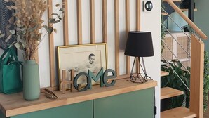 A modern interior with a wooden slat wall, a green cabinet with the word "HOME" on top, a framed picture, a lamp, and a staircase with plants. - Quiet villa with forest view  (Mios)