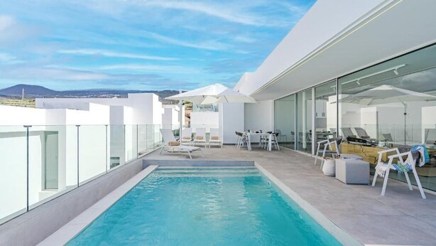 A rooftop pool area with clear blue water, white lounge chairs, and a glass-enclosed space with tables and chairs. - Villa Cala - Casangular by Upper (Adeje)