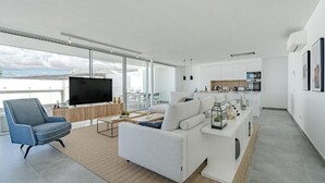 A modern living room with a sofa, TV, and a dining area with a kitchen in the background. - Villa Cala - Casangular by Upper (Adeje)
