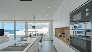 A modern kitchen with a large island, built-in appliances, and a view of the ocean. - Villa Cala - Casangular by Upper (Adeje)