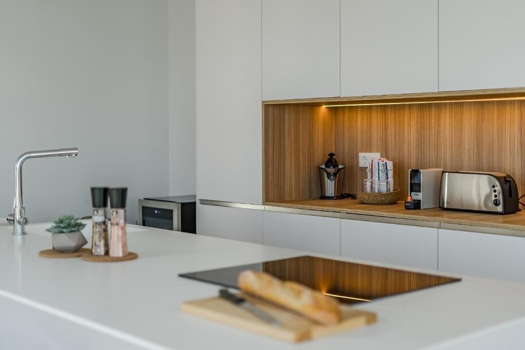 Ett modernt kök med en vit bänkskiva, en inbyggd hylla i trä, en brödrost och en kaffebryggare.