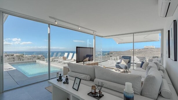 A modern living room with a large sofa, a flat-screen TV, and a view of a pool and buildings. - Villa Teresita - Casangular by Upper (Adeje)