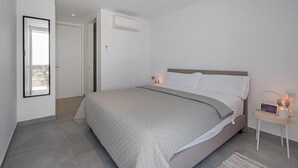 Une chambre moderne avec un grand lit, une table de chevet avec une lampe et une vue sur l’extérieur grâce à une porte ouverte.