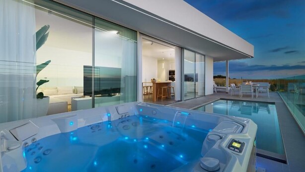 Area esterna moderna con idromassaggio, piscina e zona pranzo, il tutto visibile attraverso pareti di vetro.